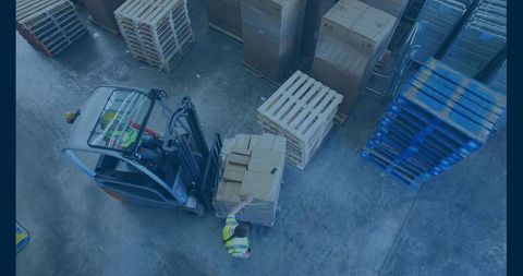 Overhead forklift operating counterbalance moving pallet with spotter guiding in warehouse