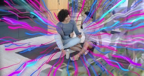 Two friends sitting and chatting on yoga mats with neon energy overlay in living room