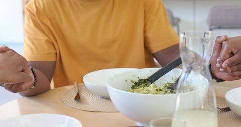 African family sharing salad and holding hands at cozy dining table, intimate meal moment