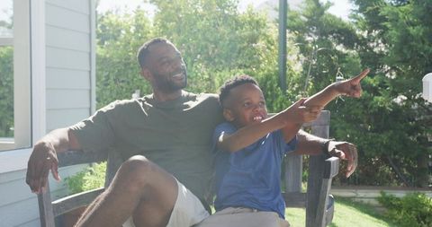 Father and son relaxing on porch bench pointing toward yard on sunny afternoon