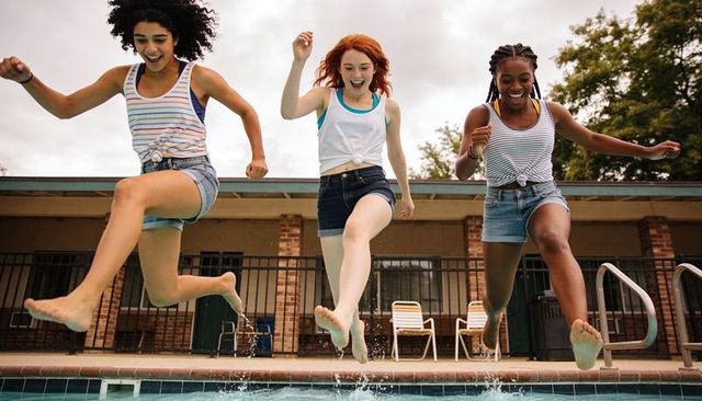 Three friends jumping into pool splashing from deck during sunny summer fun