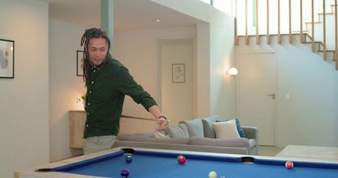 Mid-adult man lining up pool shot in modern living room with blue-felt billiards table