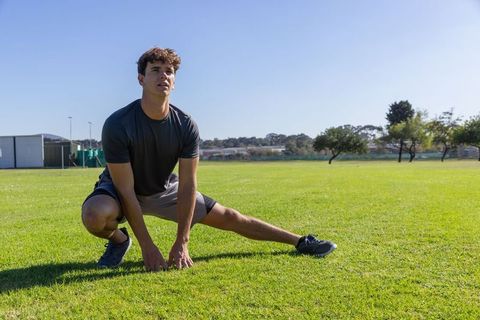 Athlete performing side lunge stretch on grassy field for outdoor fitness training