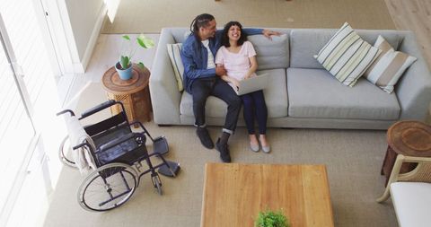 Happy Couple Relaxing in Living Room with Wheelchair Nearby - Download Free Stock Images Pikwizard.com
