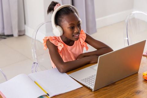 Young african girl studying online at home desk with laptop and white headphones