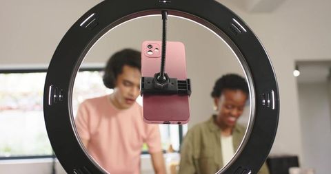 Creators collaborating around ring light recording content with pink smartphone clamp