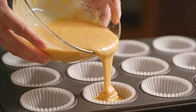 Pouring muffin batter into cupcake liners in metal pan closeup for home baking