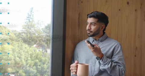 Indian Man with Mug Using Smartphone Near Office Window