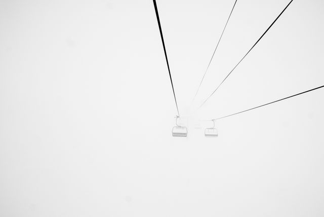 Minimalist winter scene showing a ski lift through dense fog. Ideal for themes related to winter sports, skiing vacations, or atmospheric winter landscapes. Can be useful for travel brochures, blog posts about winter adventures, or promotional material for ski resorts.