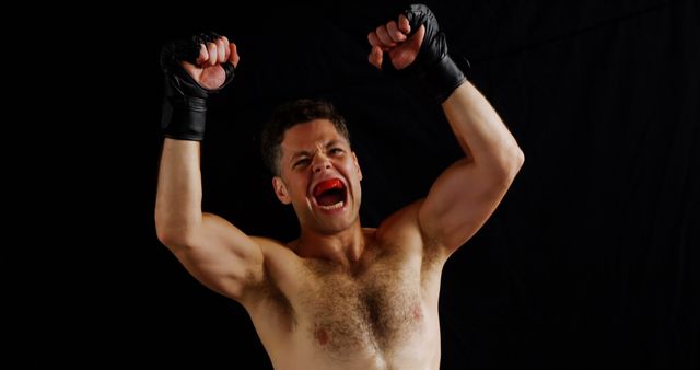 Portrait of excited male boxer posing after victory against black background