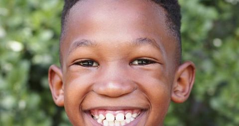 Smiling black boy close-up with sunlit garden background and floating marketing graphics