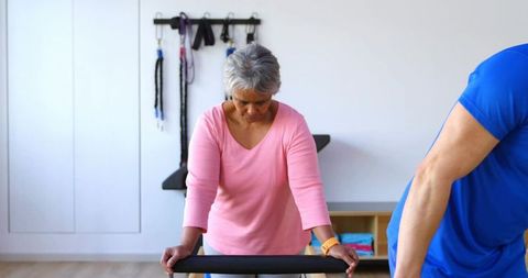 Senior woman practicing assisted balance on parallel bars during physical rehabilitation