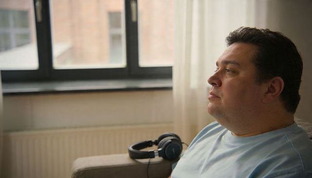 Contemplative man sitting on sofa near window with headphones, soft daylight and minimalist interior