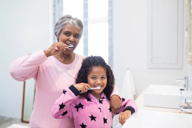 Grandmother and granddaughter engaging in a family bonding activity while brushing teeth in the bathroom. Ideal for promoting oral hygiene, family values, and multi-generational relationships. Perfect for dental care advertisements, family-related articles, and home lifestyle promotions.