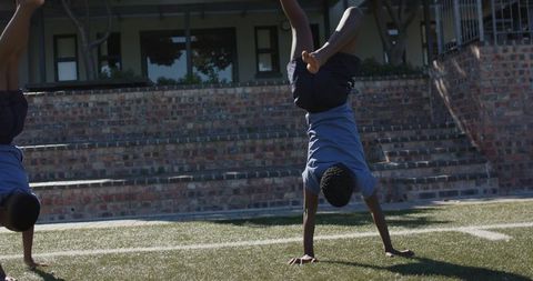 African male teenagers performing handstand and cartwheel on school turf during gym class