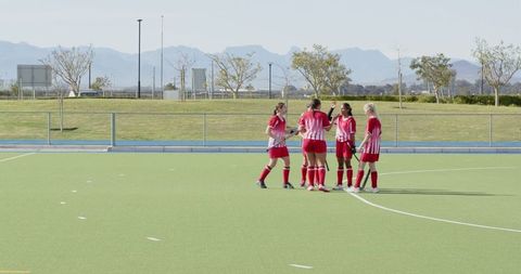 Diverse female athletes huddling on field hockey pitch