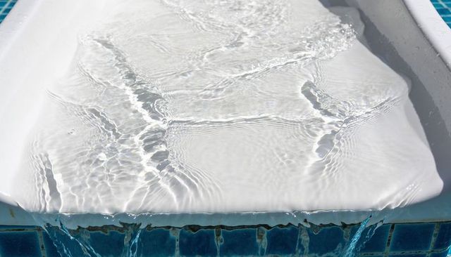 Sunlit pool scupper overflowing with rippling shallow water over blue mosaic tile edge