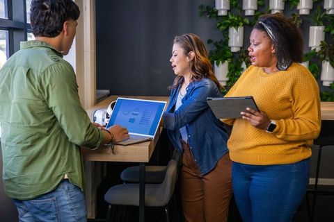 Diverse team collaborating at counter with laptop and tablet for office brainstorming