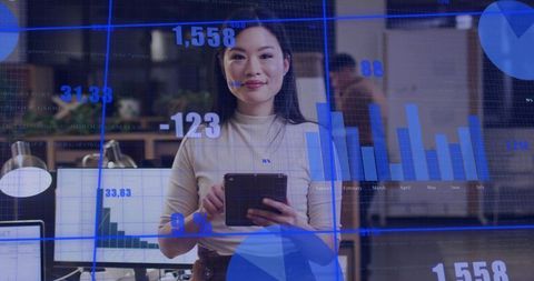 Asian professional holding tablet analyzing data charts in open office with overlays