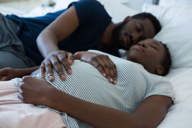 Man touching woman stomach while sleeping in bedroom at home