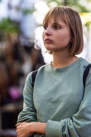 Contemplative young woman wearing green sweatshirt and backpack gazing outdoors in urban bokeh