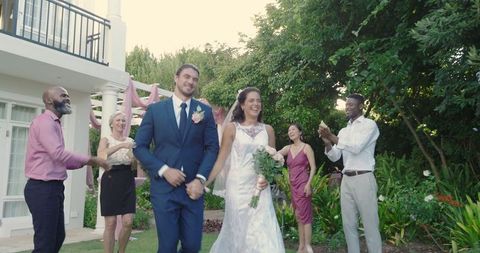 Happy bride and groom walking amidst smiling guests in garden