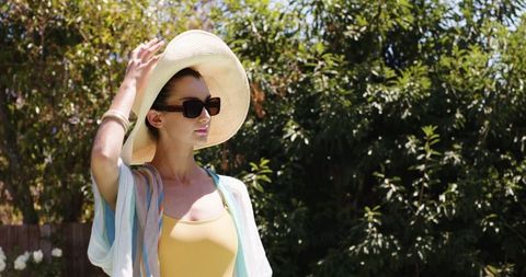 Stylish woman wearing sunhat and sunglasses posing in bright outdoors