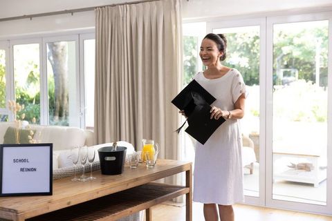 Joyful woman holding mortarboard cap at school reunion gathering