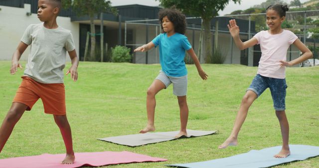 Group of kids practicing yoga poses on mats in an outdoor setting on a sunny day. They appear balanced and concentrated, participating in a fun and healthy activity. This can be used to promote children's fitness programs, outdoor activities, and healthy living.