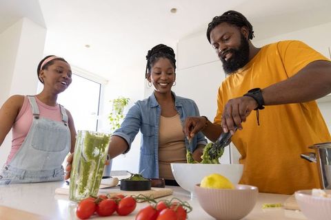 African family cooking together in bright modern kitchen preparing green pesto