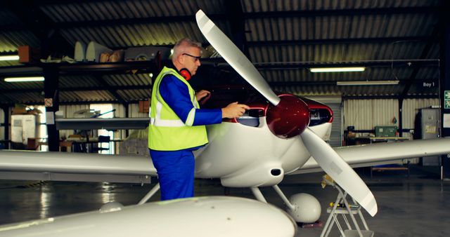 Aircraft mechanic performing maintenance on a propeller plane in an aircraft hangar. Ideal for use in articles about aviation maintenance, technical jobs in aviation, or showcasing the role of a mechanic in an airport hangar.