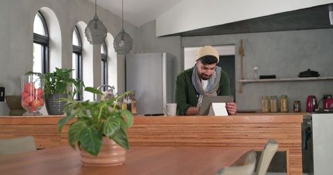 Indian man using tablet in cozy modern kitchen standing behind wooden counter with plants