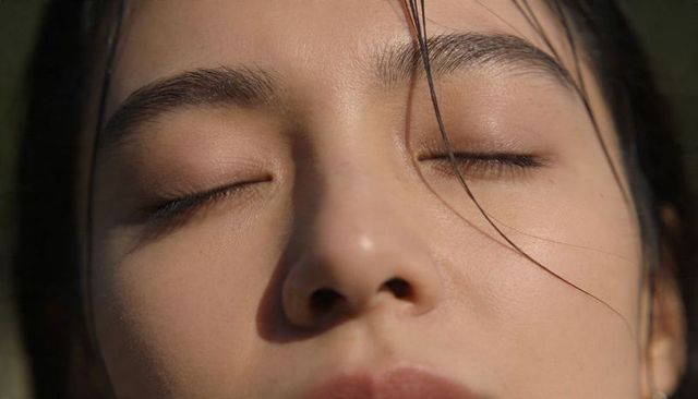 Closeup asian woman bathing in warm sunlight with closed eyes and natural skin texture