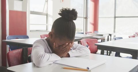 Young Student Frustrated at School Desk in Classroom