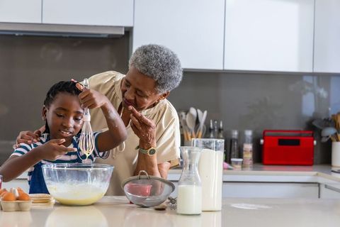 African american grandmother teaching granddaughter baking at modern kitchen island