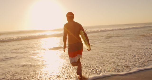 Man walking towards ocean carrying surfboard at sunset, with waves and horizon in background. Bright sunlight reflecting on water and sand, creating serene atmosphere. Ideal for beach lifestyle themes, surfing, summer activities, outdoor adventures, freedom concept, relaxation, and vacation promotions.