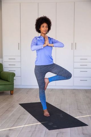 Focused woman practicing yoga tree pose at home