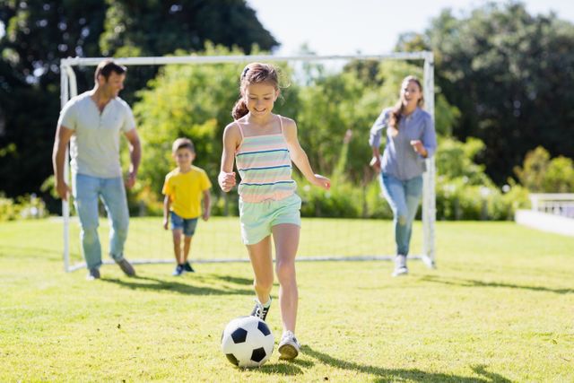 Family enjoying a sunny day in the park playing soccer together. Ideal for promoting family bonding, outdoor activities, and healthy lifestyles. Perfect for use in advertisements, brochures, and websites related to family activities, sports, and outdoor fun.