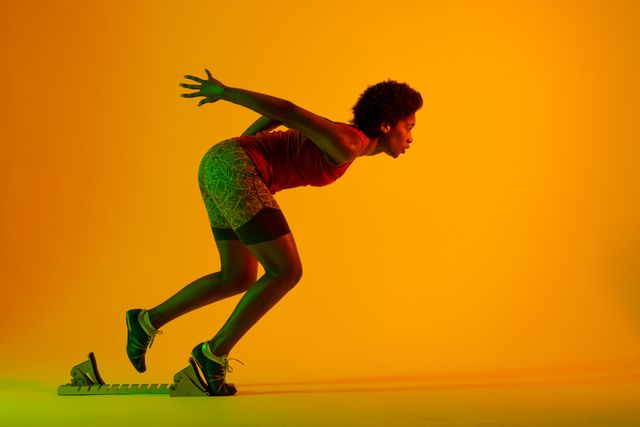 Side view of african american female player with afro hair running over neon yellow background. Copy space, sport, competition, exercise, fitness and active lifestyle concept.