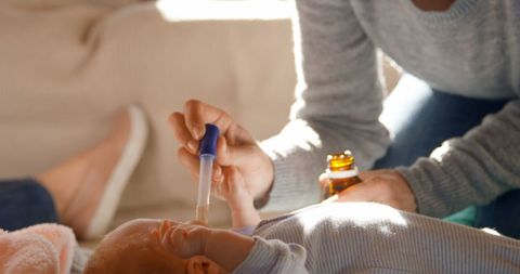 Mother Giving Medicine to Infant with Dropper at Home