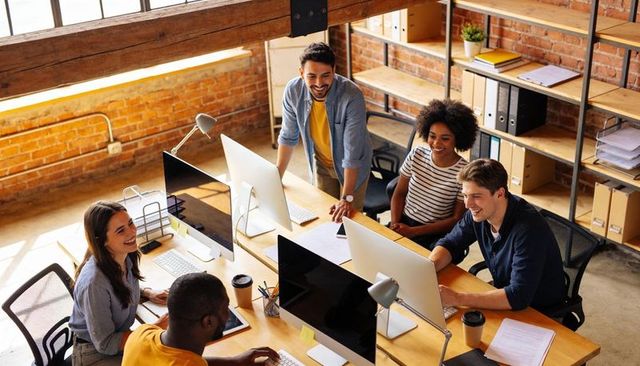 Creative startup team collaborating around desktop computers in sunlit brick loft office