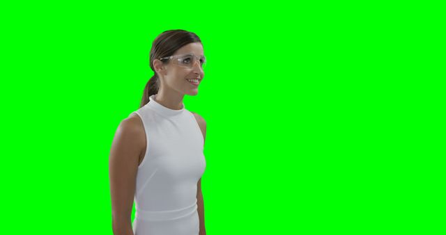 A woman in white outfit is seen smiling while wearing protective glasses against a green screen background. This visual can be used in technology marketing materials, safety training videos, professional presentations, or as a placeholder for virtual application backgrounds.