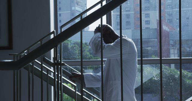 Depicts a doctor feeling stressed standing in a hospital stairway. This can be used in articles or websites discussing mental health of medical professionals, challenges faced by healthcare workers, work-life balance concerns, or the impact of stressful work environments on doctors.