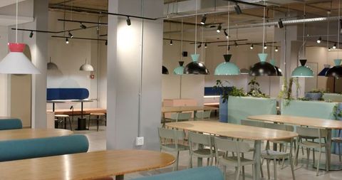 Modern coworking lounge featuring pastel pendant lights, wooden tables and plants
