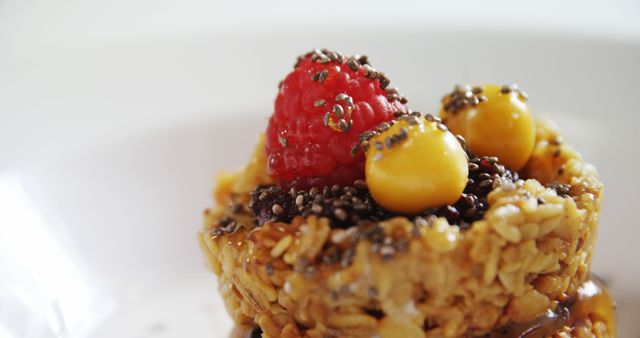 A close-up of a granola cup topped with a fresh raspberry, chia seeds, and golden berries, with copy space. Its vibrant colors and textures suggest a focus on healthy and visually appealing food options.