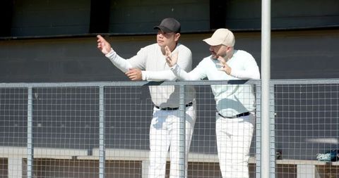 Two coaches leaning over dugout railing pointing and gesturing during baseball game
