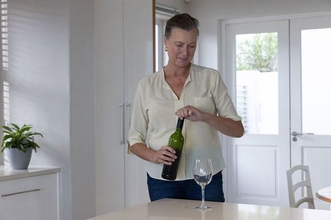 Mature woman opening wine bottle in modern kitchen