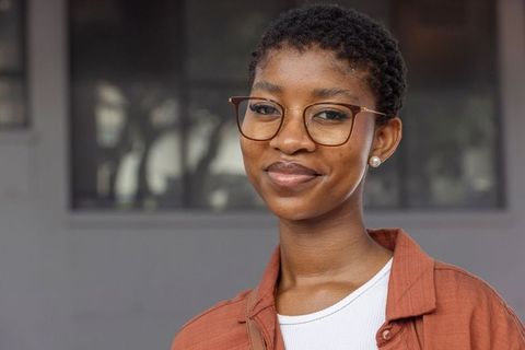 Confident african woman wearing tortoiseshell glasses and rust jacket smiling urban portrait