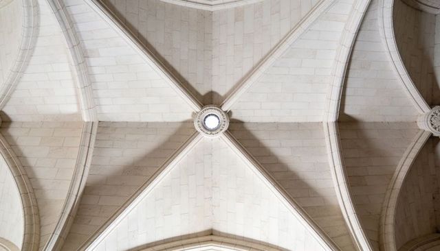 Central gothic ribbed vault featuring circular boss and ocular light in limestone nave