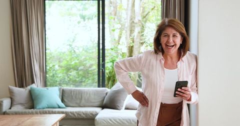 Senior Woman Laughing with Smartphone in Contemporary Home Interior